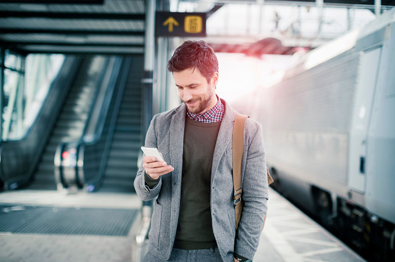 30-something guy texting in a train station with the train waiting beside him.
