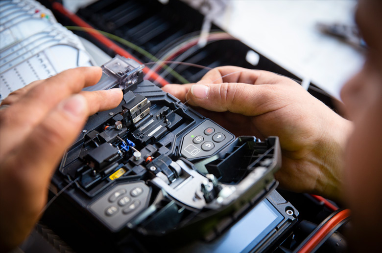 Closeup of two hands 'welding' two fiber optic cables together with a portable fiber optic welding device.